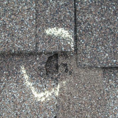 Close-up of asphalt shingle roof with chalk circle marking hail damage and cracked shingle