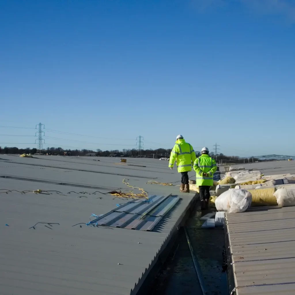 2 men in high-vis and hard hats performing a roof inspection of a metal commercial roof