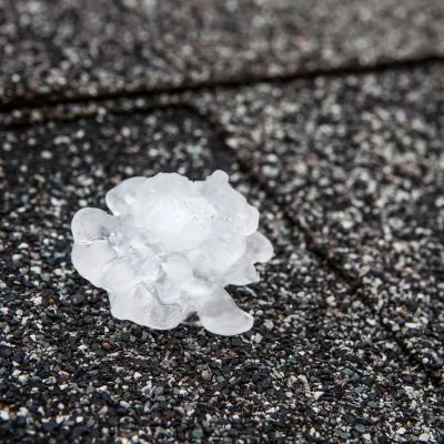 Large hailstone on black, asphalt shingle