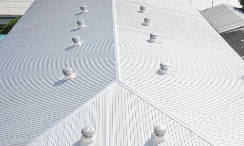 Top view of a white metal commercial roof with multiple ventilation caps evenly spaced along the ridges