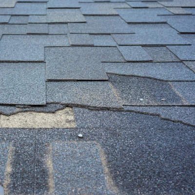 Close-up of damaged asphalt roof shingles showing wear, deterioration, and lifting edges that require repair or replacement.