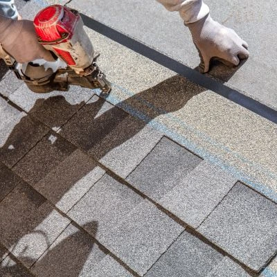 Close-up of a roofing professional installing asphalt shingles using a pneumatic nail gun.