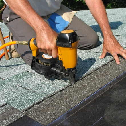 A Moore and Sons crew member installing shingles on a home with a nail gun.