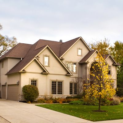 A beige stucco two-story house with new Owens Corning shingles with a garage, gabled roofs, and a driveway.
