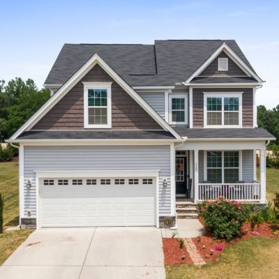 A two-story suburban house with gray Owens Corning shingles, a white garage door, a covered front porch, and brown siding.