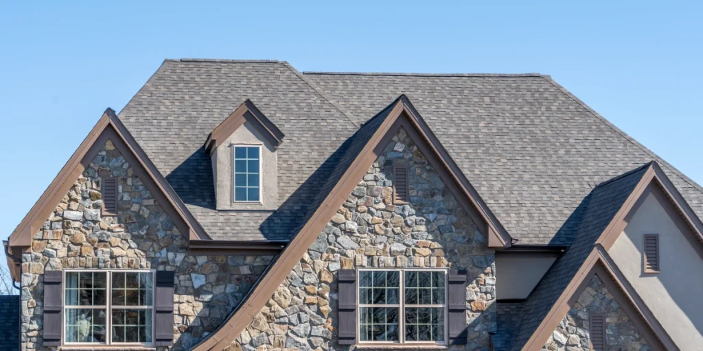 A luxury stone house featuring a complex multi-gabled roof with high-quality architectural asphalt shingles and decorative dormer windows.